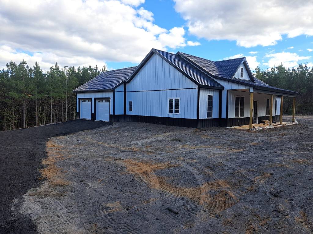 Working description: a large white house in the countryside on a cloudless but overcast day. Two white garage doors, and a...
