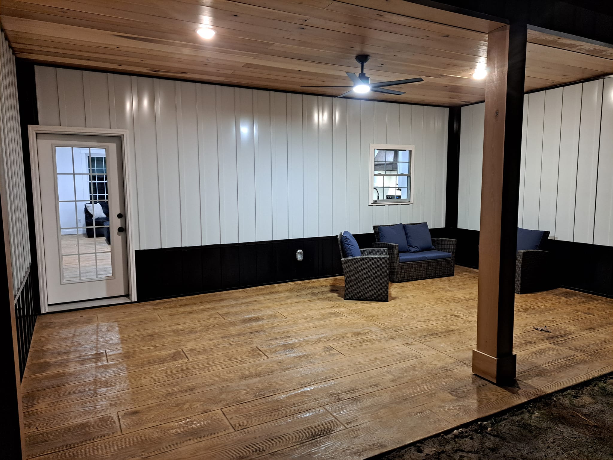 A spacious room with white and black paneled walls, a wooden floor, and a smooth dark gray floor-to-ceiling partition that...