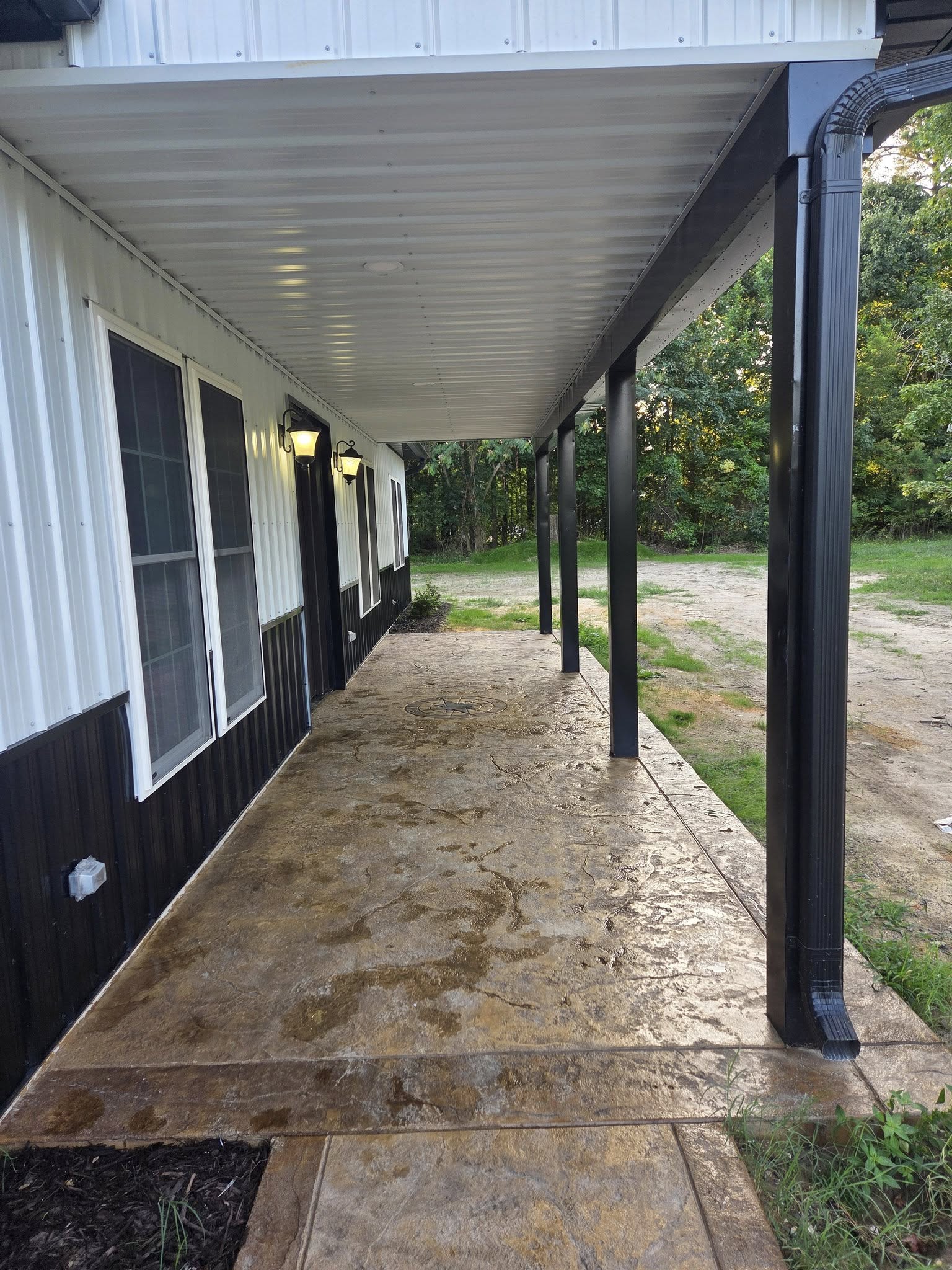 A covered porch located on a white and black ranch-style building with an outdoor black gutter system.