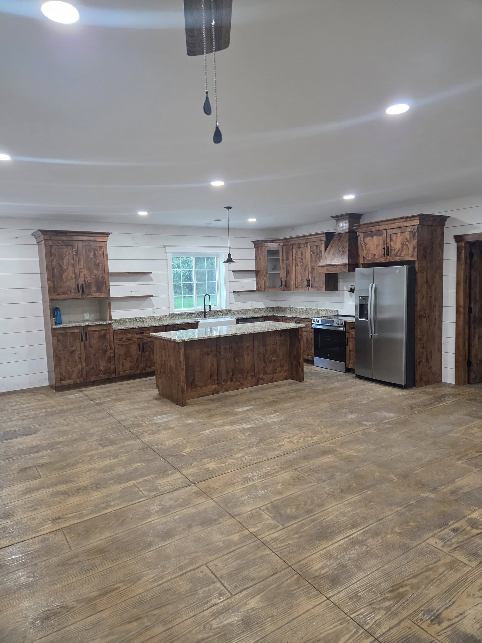 A modern kitchen with wooden cabinets and granite countertops. It features a large central island, stainless steel refrige...
