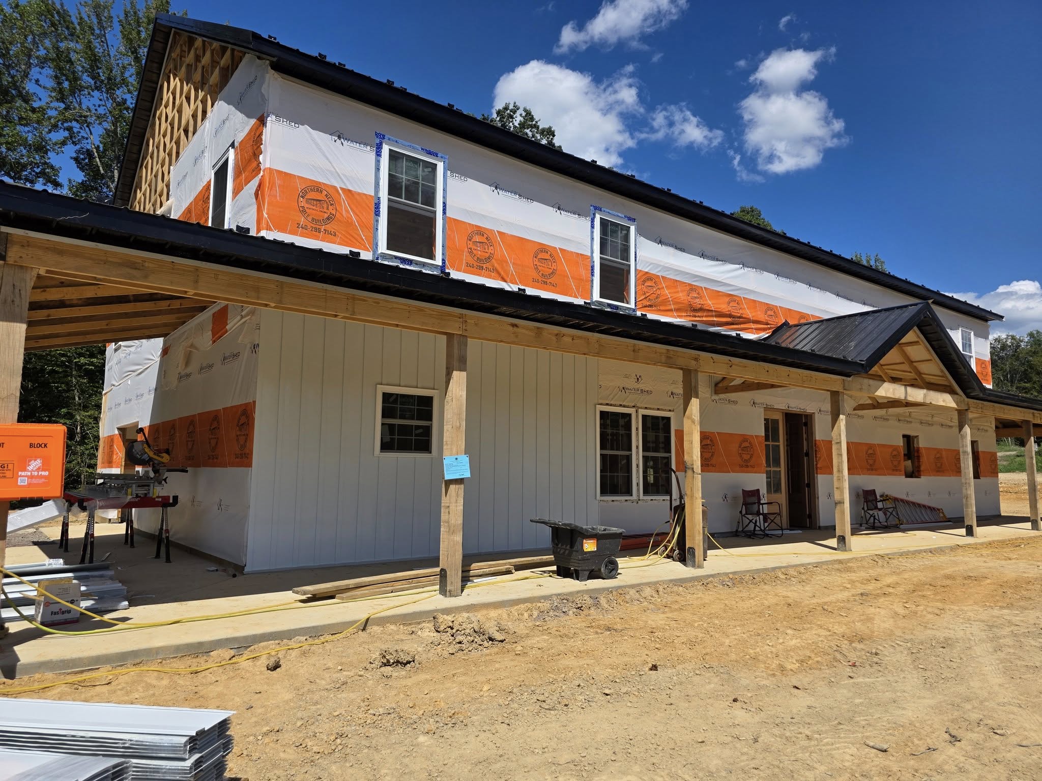 Newly built house under construction, with orange and white protective covering on exterior, and black roof, set against a...